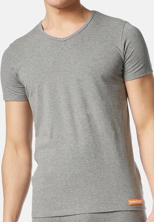 Mand iført en tætsiddende grå T-shirt med kort ærme og V-hals, der har et lille orange mærke på den nederste venstre side.