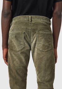 Pantalones de pana verde olivo con corte recto, que cuentan con dos bolsillos traseros y una textura visible del tejido acanalado.
