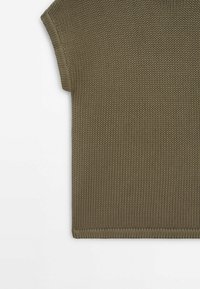 Gros plan sur un haut sans manches en maille vert olive, se concentrant sur la partie supérieure gauche, montrant la texture détaillée du tricot et l'emmanchure.