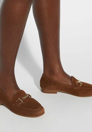 Bruine suède instappers met een lage hak, voorzien van een goudkleurig hardware accent aan de voorkant en een gladde, textuurachtige oppervlakte.
