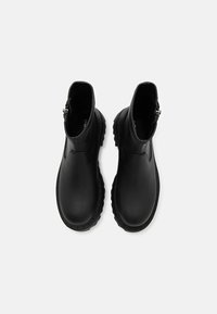 Bottines noires avec une finition en cuir lisse, des côtés élastiques, et une semelle en caoutchouc texturée, dotées d'une fermeture éclair à l'arrière.