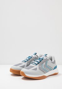 Grijze sportschoenen met een bovenkant van mesh, blauwe accenten, getextureerde overlay en witte veters. Voorzien van een rubberen zool in een contrasterende oranje kleur.