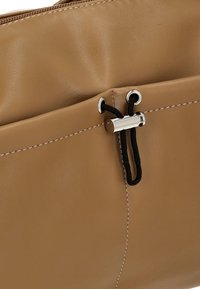 Tan leather handbag with smooth texture, featuring a zip closure, black cord detail, and contrasting stitching for added accent.