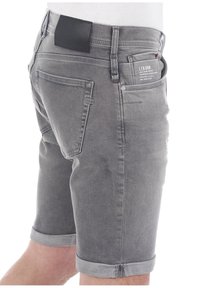 Pantalones cortos de mezclilla gris de corte ajustado, con dobladillos enrollados, detalle en el bolsillo trasero y una etiqueta de cuero negro en la cinturilla.