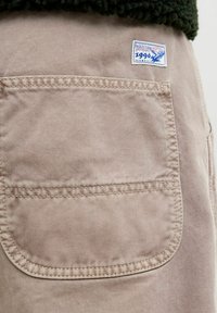 Beżowe bawełniane szorty cargo z zaokrągloną tylną kieszenią oraz niebieską łatą z logo "Jack & Jones 1990" z motywem orła.