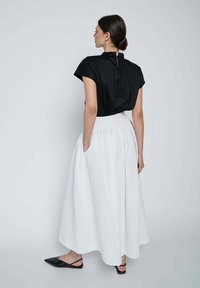 Black short-sleeve top with a back keyhole, paired with a white textured, pleated floor-length skirt. Black pointed flat shoes.