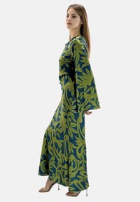 Længde, flydende kjole med en mørkeblå bund og store grønne blomsterkonstruktioner. Lange klokkeærmer og en tætsiddende liv betoner designet.