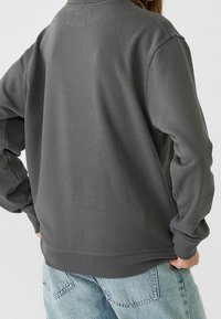 Sudadera gris de corte relajado, con puños y dobladillo acanalados, fabricada en material suave. Presenta un diseño liso sin patrones visibles.