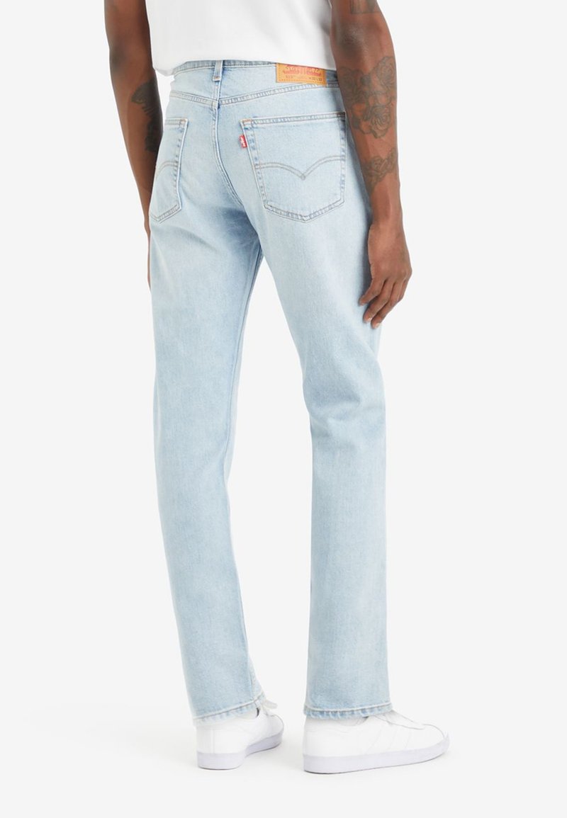 Lichtblauwe denim jeans met een rechte pijp, voorzien van achterzakken en een tan leren label op de tailleband. Draag ze met witte sneakers.