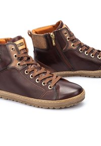 Zapatillas altas de cuero marrón con ojales dorados, cordones marrones, un cierre lateral y acentos texturizados en tono beige en el cuello y la suela.