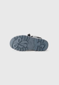 Suela de zapato negra con un material de goma azul texturizado que presenta un patrón de corazones y una correa ajustable. Tamaño 27 indicado en la parte inferior.