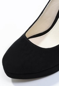 Sort suede pumpe med rund tå og lav platform. Glat indvendig foring, enkelt design og syede kantdetaljer.