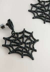 Gli orecchini a forma di ragnatela nera presentano un design a trame dettagliato con accenti luccicanti. Un gancio in metallo è attaccato per un'indossamento sicuro.