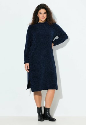 Navy blue knitted dress with long sleeves and a high neckline; features side slits. Paired with black ankle boots. Textured finish.