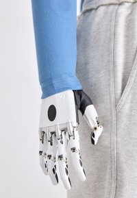 Robotizirana proteza ruke sa srebrnim i crnim dizajnom. Sadrži artikulirane prste s vidljivim zglobovima i okrugli kontrolni gumb.