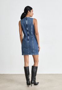 Denim uten ermer kjole, tettsittende med vertikale sømmer, lys blå vask, midt på låret lengde, og høy hals, kombinert med svarte knelengde støvler.