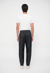 Pantalones deportivos negros de corte holgado, con cinturilla elástica y franjas laterales, combinados con una camiseta blanca sencilla y zapatos de color claro.