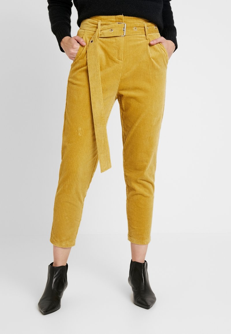 Gula kordflorbyxor med bälte i midjan, kortade ben och framfickor. Matchas med svarta ankelboots för en komplett look.