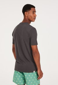 Grå bomuld t-shirt med korte ærmer, rund hals og normal pasform, parret med grønne badebukser med subtile palme mønstre.