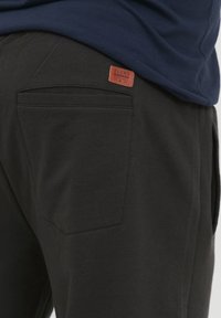 Sorte joggebukser laget av myk stoff, med en baklomme og et brunt lærmerke merket "BLEND." Designet er enkelt og funksjonelt.