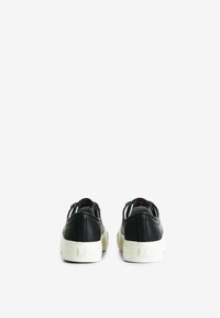 Sneaker in pelle nera con suole in gomma bianca, caratterizzati da una texture liscia, forma arrotondata e design minimalista. Accento rosso all'interno.