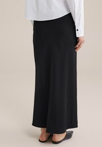 Gonna maxi nera realizzata in tessuto leggero, con una texture liscia e una silhouette dritta. Abbinata a scarpe nere senza lacci.