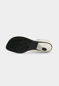 Sandale blanche à talon pour femme vue de la semelle, avec une semelle extérieure en caoutchouc noir texturé et un talon fin avec embout antidérapant.