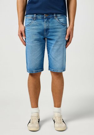 Denim shorts in light blue with a regular fit, five pockets, and frayed hem. Worn with white socks and beige athletic shoes.