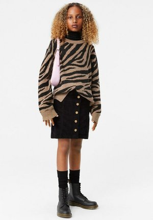 Maglione a righe zebra marrone e nero, gonna in corduroy nera con bottoni dorati, calze nere fino al ginocchio e stivali neri con lacci. Borsa rosa.