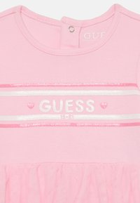 Abito rosa con top in cotone caratterizzato da un logo "GUESS" glitterato e strisce, e gonna in tulle. Chiusura a scatto al collo.