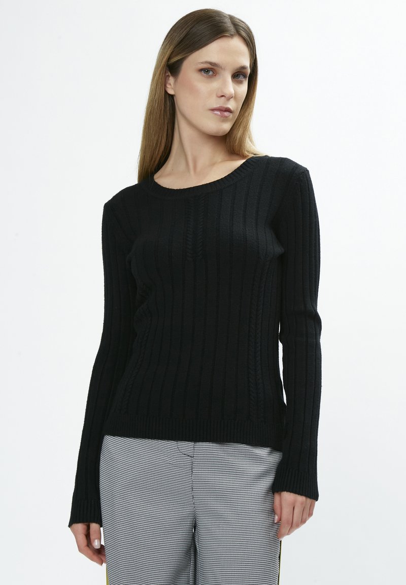 Schwarzer gerippter Strickpullover mit langen Ärmeln, runder Ausschnitt und auffälligen vertikalen Mustern. Kombiniert mit karierter Hose.