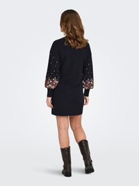 Black dress with floral-embroidered, colorful puff sleeves and solid back, paired with brown knee-high boots and a slightly fitted silhouette.