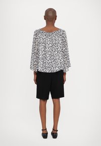 Bluse med blomstertrykk i svart og hvitt, løs passform med vid hals, kombinert med svarte shorts. Fottøyet har naglede detaljer.