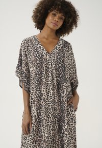 Kaftan s leopardím vzorom s výstrihom do V, krátkymi rukávmi a bočnými vreckami. Vyrobený z ľahkej tkaniny so svojou jemnou, prúdiacou textúrou.