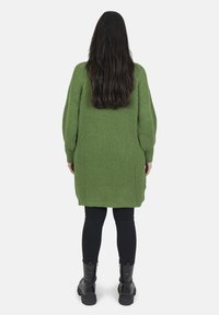 Lungo, spesso, maglione a costine di colore verde oliva, con spalle cadenti. Indossato sopra leggings neri e stivaletti neri.