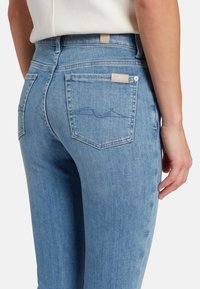 Jeans in denim blu chiaro con una vestibilità slim. Presentano tasche posteriori e dettagli di cucitura discreti. Il materiale sembra morbido con un leggero effetto usurato.