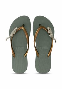 Tongs vertes en caoutchouc avec une semelle texturée, des sangles en bronze et une décoration en lézard en argent sur chaque sangle.