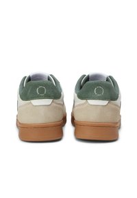 Zapatillas blancas con acentos de ante verde en el talón y lados de ante beige. Presentan una suela de goma texturizada en tono marrón y un detalle de logo circular en el talón.