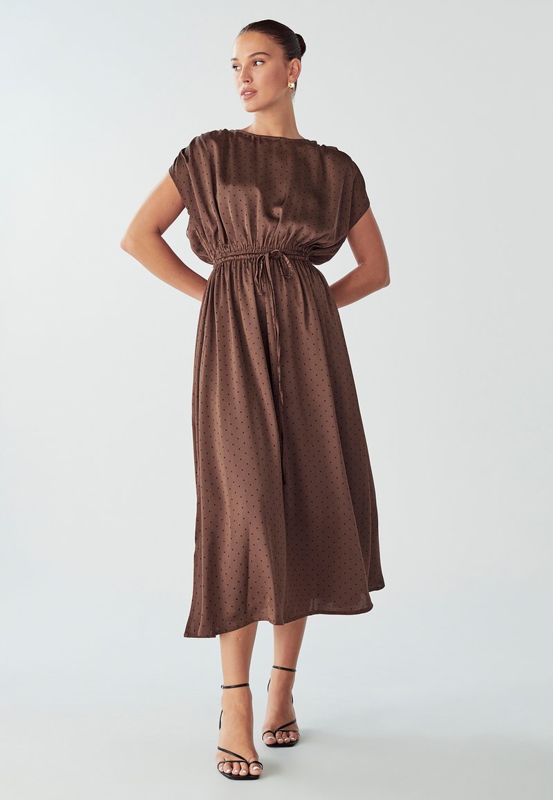 Bruine jurk met stippen, in een ontspannen pasvorm, korte mouwen en een elastische taille. Soepele stof met een middellange zoom en minimale accenten.
