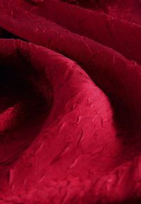 Tissu rouge profond avec des plis doux et une surface texturée légèrement froissée créant des contrastes de lumière et d'ombre.