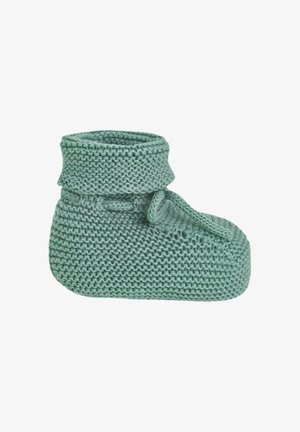 Petit chausson vert tricoté pour bébé avec revers plié et bride à l'avant sur fond blanc.