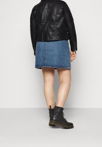 Veste en cuir noire, jupe en denim bleu, bottes noires à lacets. Matériau lisse, design ajusté, jupe longueur genou, et détails de surpiqure contrastants.