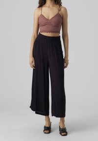 Kvinna som bär en mauve virkad crop-top, svarta vida byxor, svarta klacksandaler med rosett och ett guldarmband på vänster handled.