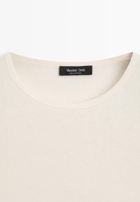 T-shirt couleur crème à col rond avec une étiquette noire Massimo Dutti cousue à l'intérieur du col arrière, fabriquée au Portugal.