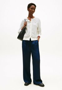 Cardigan a righe in crema e navy, con chiusura a bottoni, abbinato a pantaloni navy a vestibilità ampia. Una borsa nera completa l'outfit.