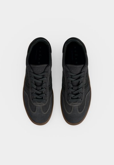 Paire de baskets décontractées gris foncé avec des lacets noirs et des semelles marron, vues de dessus sur un fond clair uni.