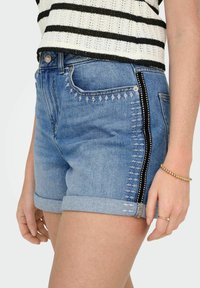 Shorts in denim con orlo arrotolato, lavaggio azzurro chiaro, striscia nera laterale con cucitura bianca e cuciture decorative sulle tasche anteriori.