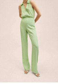 Combinaison verte avec col, présentant un motif géométrique, design sans manches et coupe jambes larges. Tissu texturé avec une finition lisse.