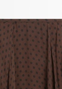 Tissu marron à pois noirs avec des plis doux et une surface texturée.