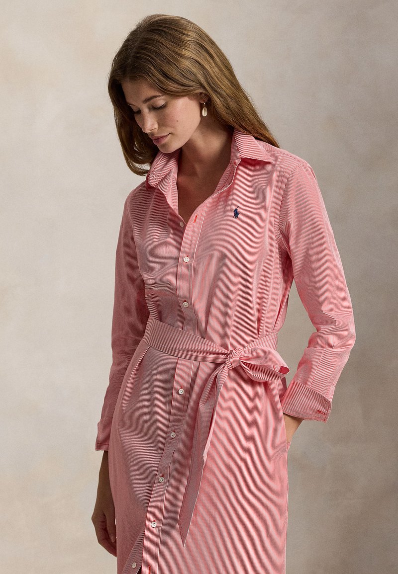 Ριγέ φόρεμα σε κόκκινο και λευκό, κ ατασκευασμένο από ελαφρύ ύφασμα, με κουμπιά μπροστά, μακριά μανίκια και ζώνη στη μέση που δένει.